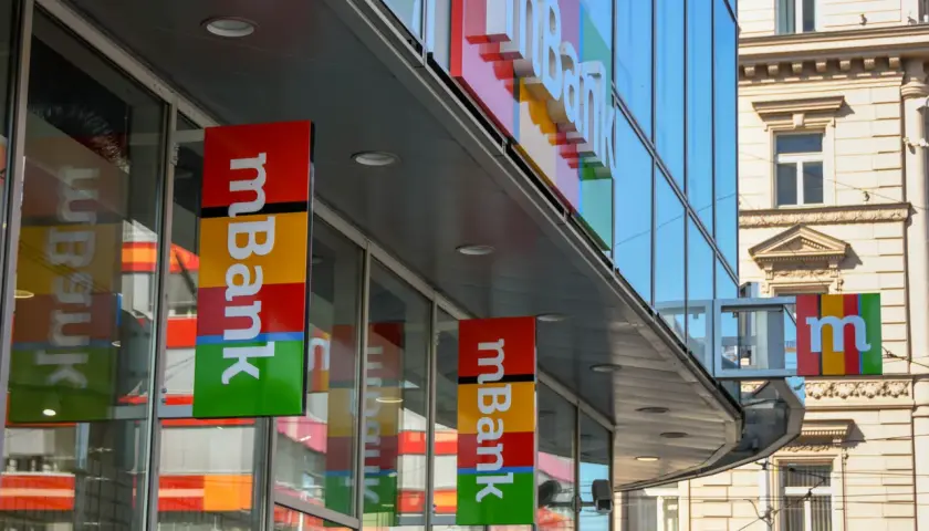 Baner mBank z kolorowym logo i napisem "mBank" na tle nowoczesnego budynku.